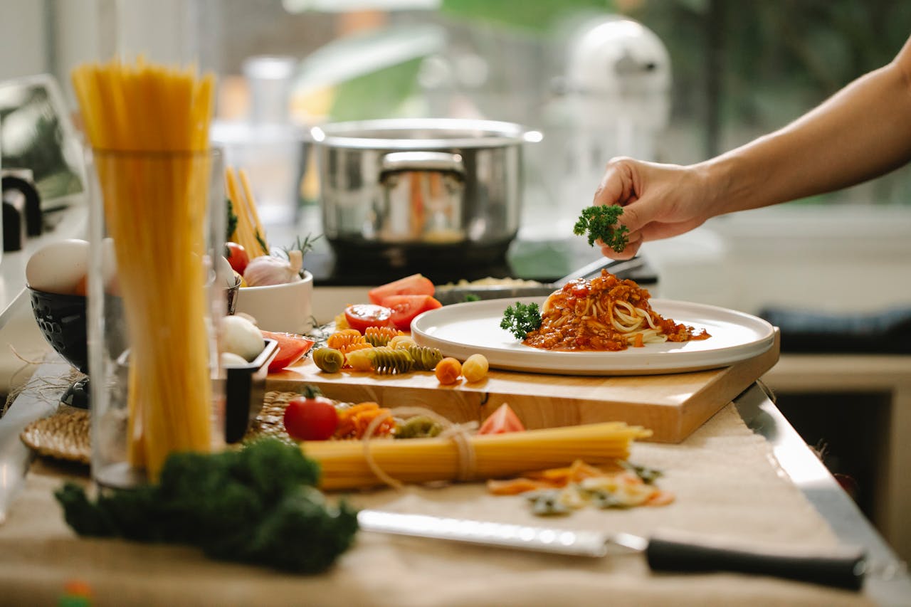 Crop anonymous chef adding parsley to spaghetti with tomato and meat while cooking lunch in kitchen