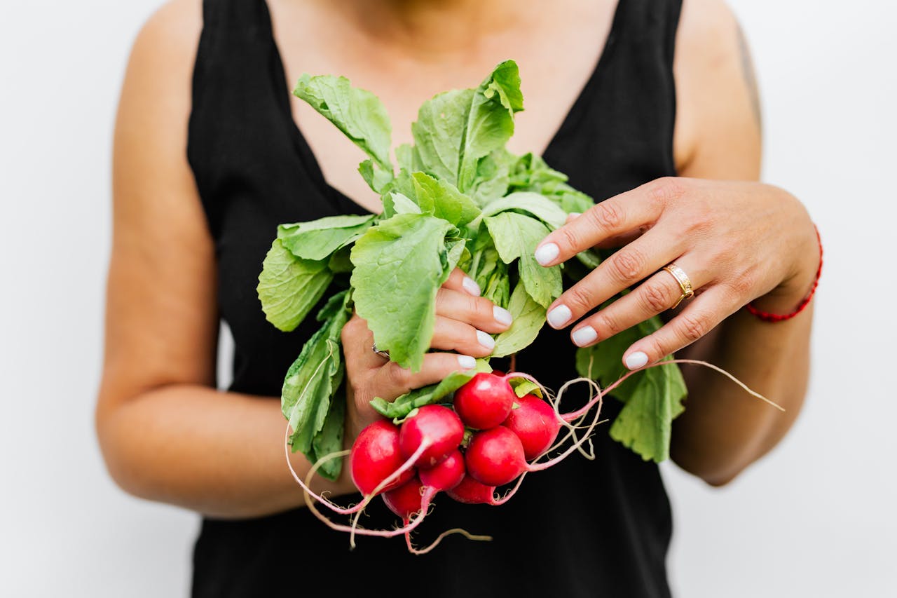 A person holding fresh radishes with vibrant green leaves against a white background.